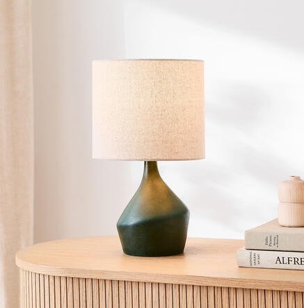 Handcrafted ceramic lamp with organic curves and a modern silhouette — perfect for balanced, artistic light. Sculptural asymmetry ceramic table lamp with linen shade on mid-century wood nightstand.