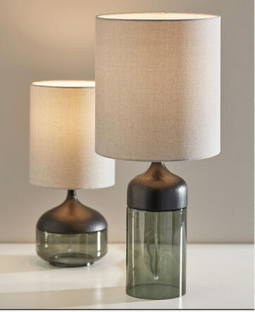 Smoked glass and black wood table lamp with light gray linen shade on bedside table in modern neutral bedroom. A sleek mix of smoked glass and black wood with a soft linen shade. Perfect for adding depth and mood to your bedside or dresser.