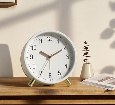 Round minimalist metal alarm clock with gold frame and white face, sitting beside a stack of books.