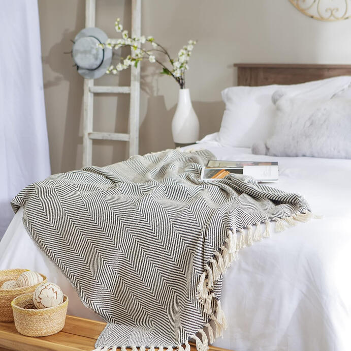 Neutral cotton throw blanket with fringe detail, draped over a chair. Adds natural texture and rustic warmth to a mid-century modern bedroom.