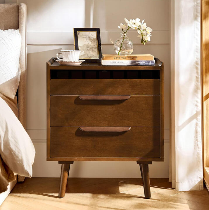 Walnut mid-century nightstand with USB charging ports and pull-out shelf, styled beside a cozy neutral bed.