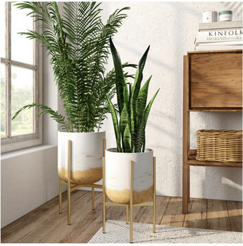 Pair of white and gold mid-century modern planter stands with slim gold legs, styled indoors with soft greenery. Elegant modern design for bedrooms or living spaces.